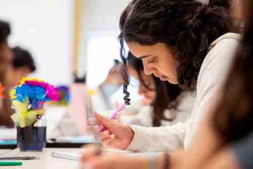 Student leans over a piece of paper, writing