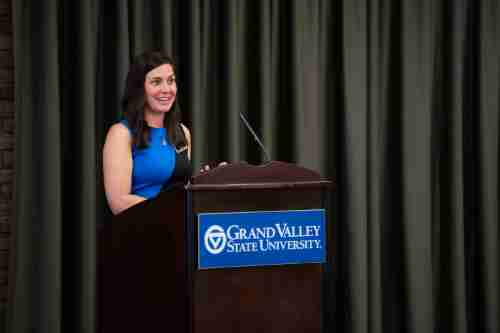 Woman in blue stands at a podium with 'Grand valley State University' logo on it