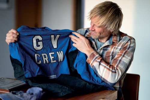 Ben Moon sits at a table and hold up his old GV Crew jersey