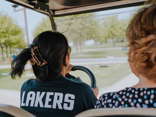 Devina drives a golf cart. We see the back of her shirt which reads LAKERS in large letters