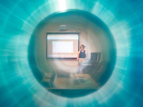 A view through a blue circular burst that fogs and hazes over part of the center image which is Hannah standing at the front of a classroom explaining something