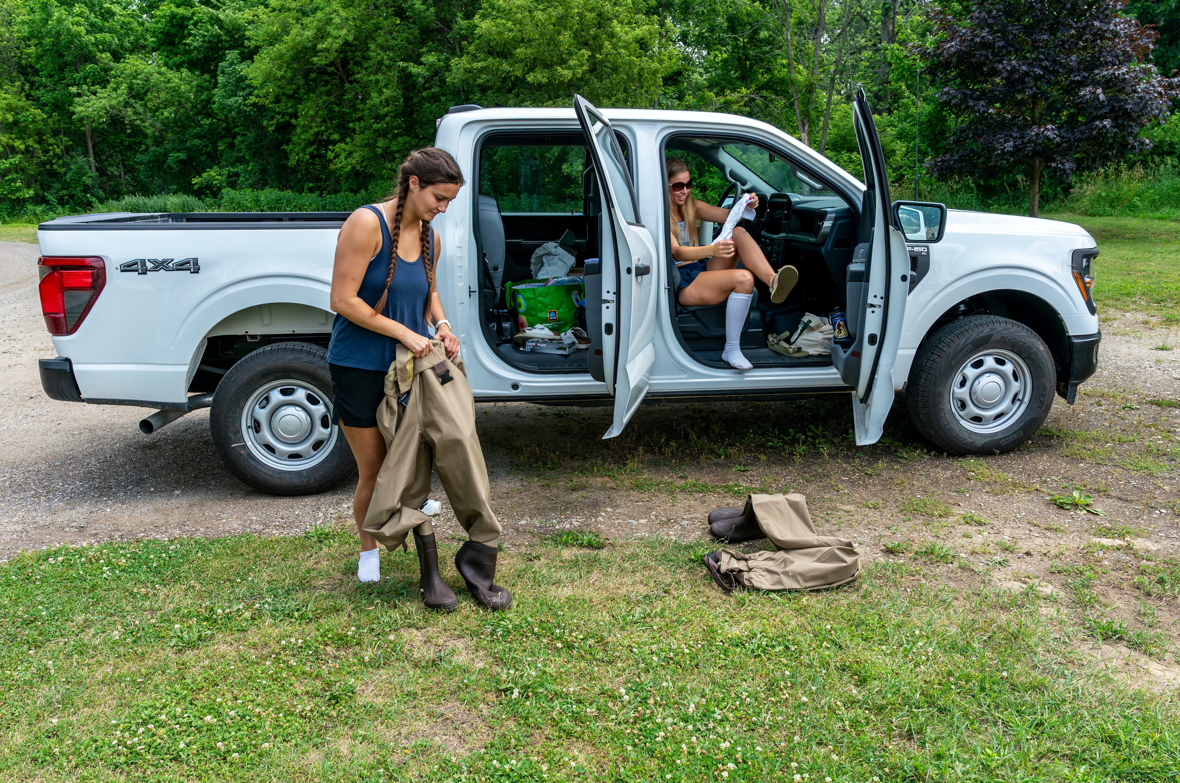 students near white pickup truck putting on waders to go into a river