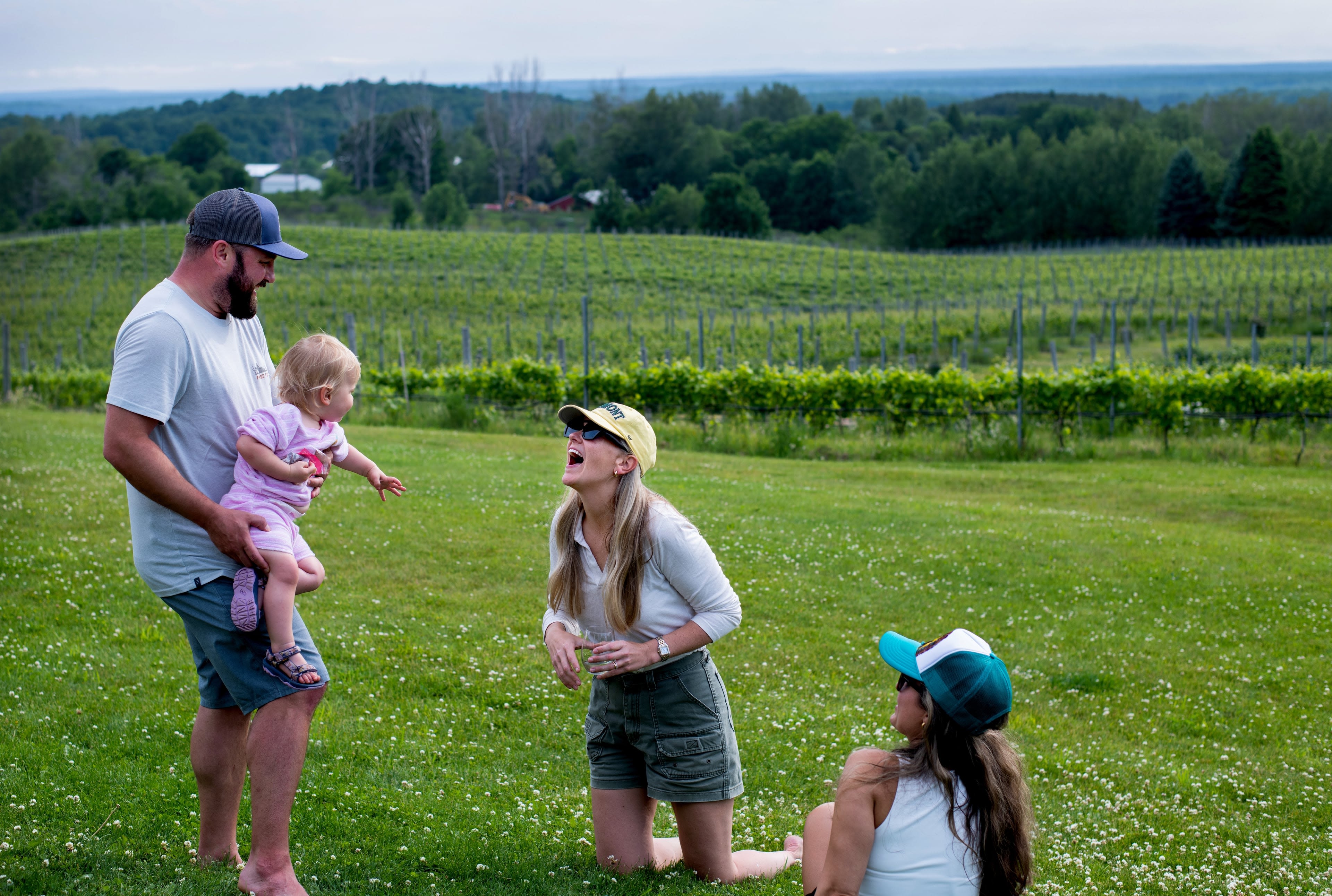 a family plays outside in the grass with the vineyard in the background