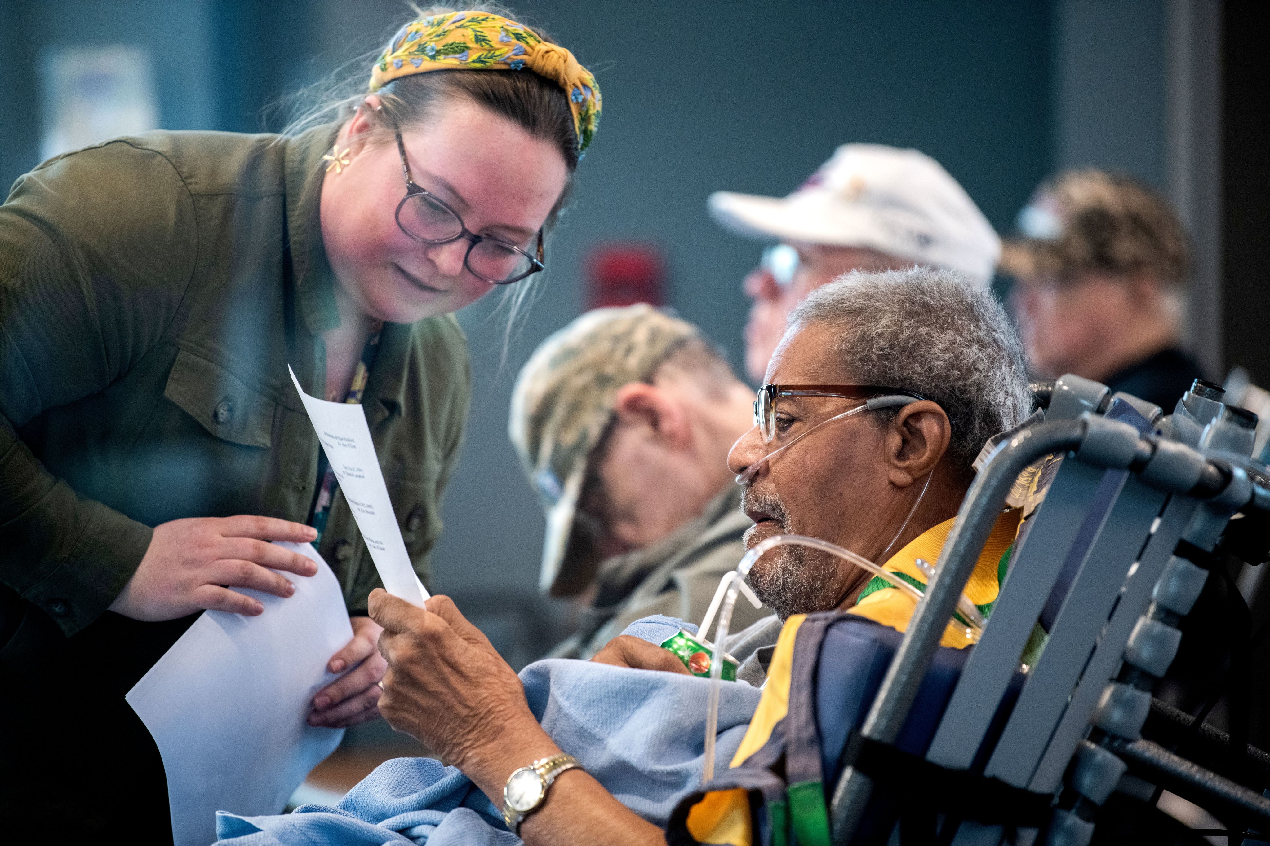 a woman leans to answer a question from a man in a wheelchair with oxygen tubes 