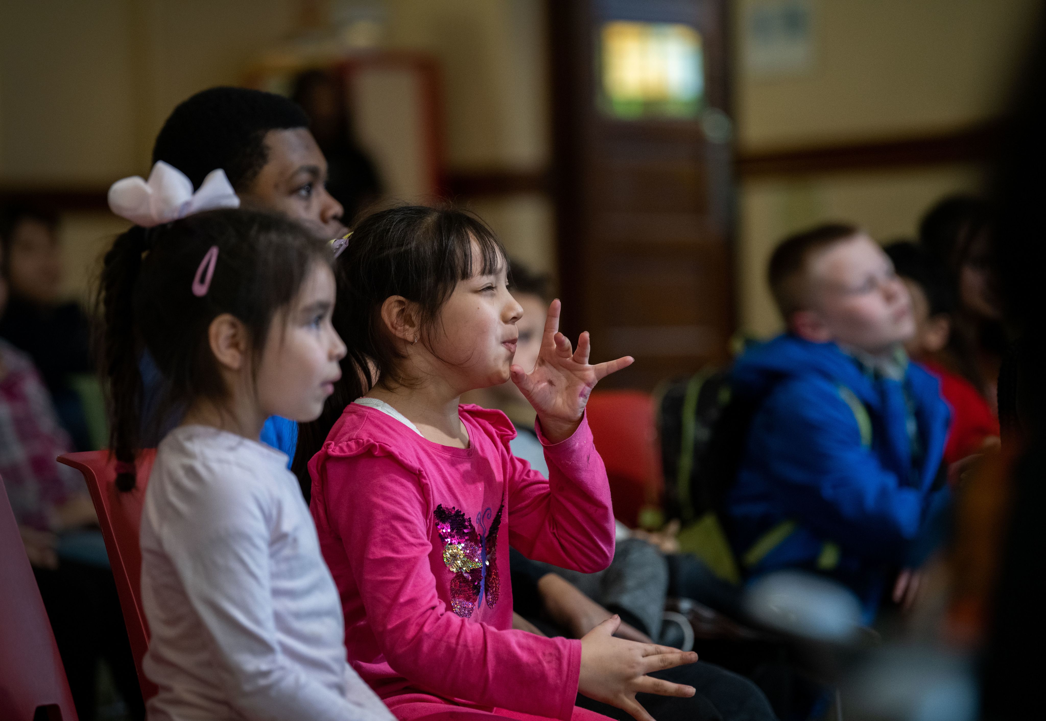 young students watch concert, girl in pink shirt pretends to blow horn