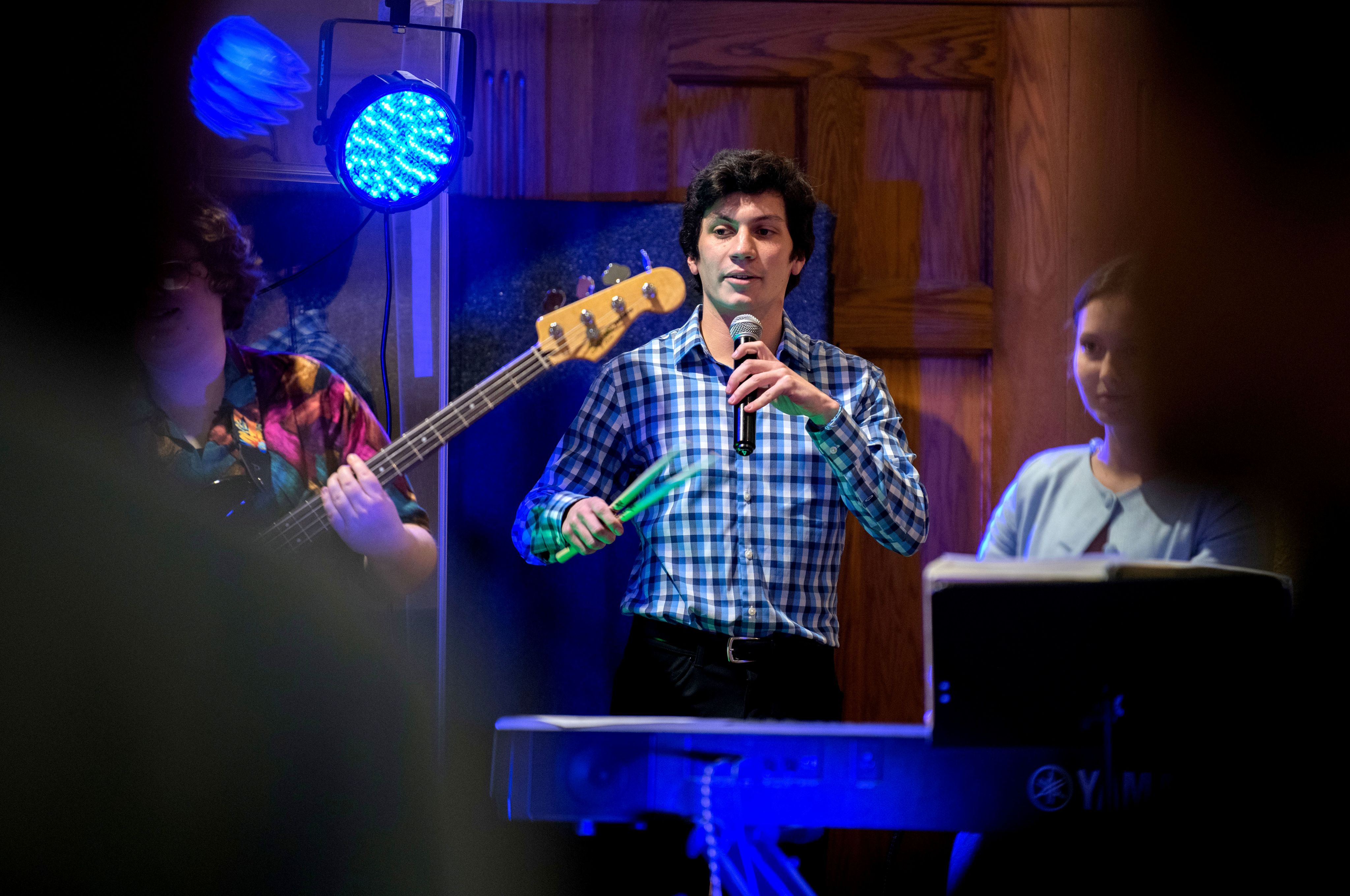 band with person in checked shirt holding microphone and drum sticks in center