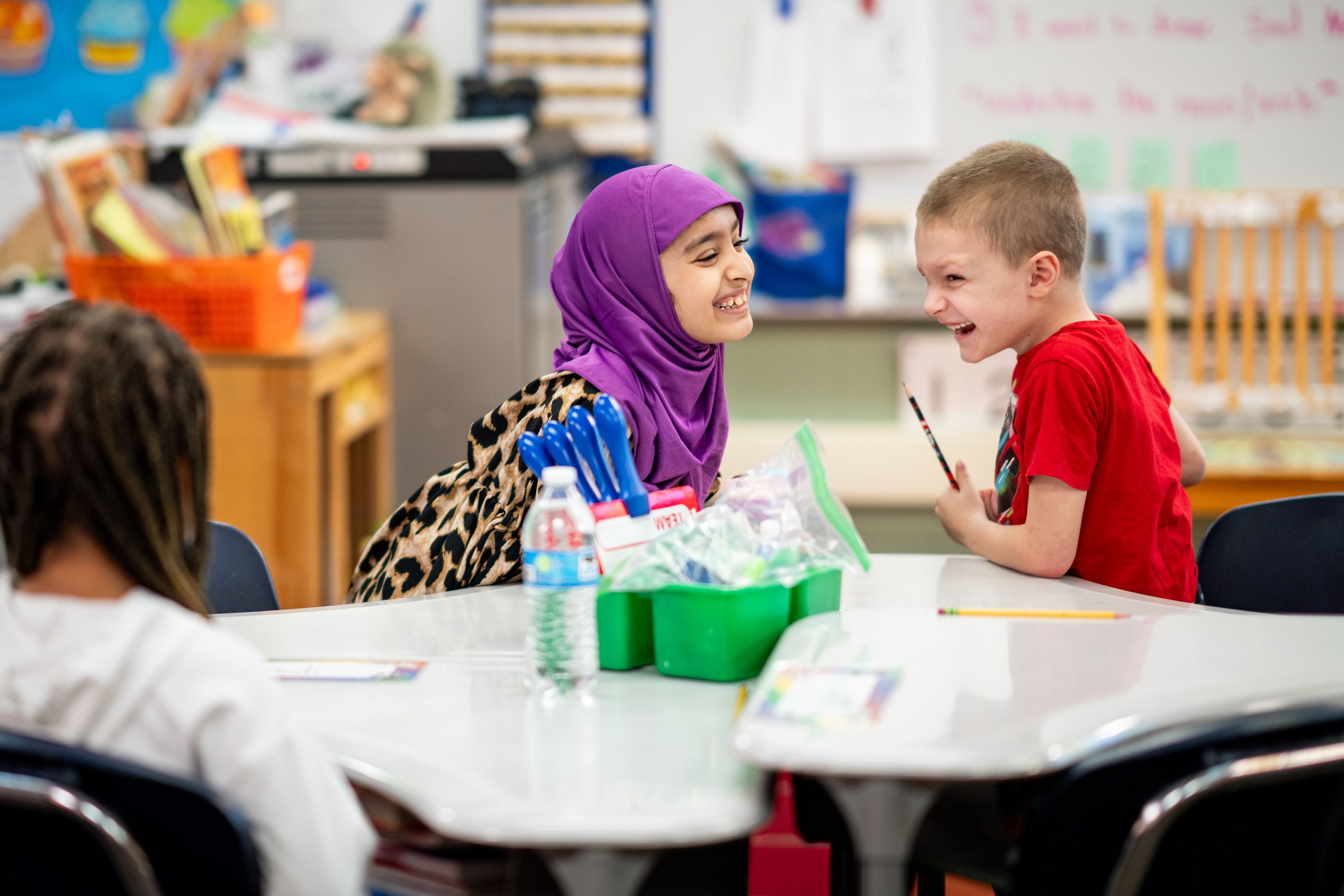 two young elementary students laugh together while seated at tables