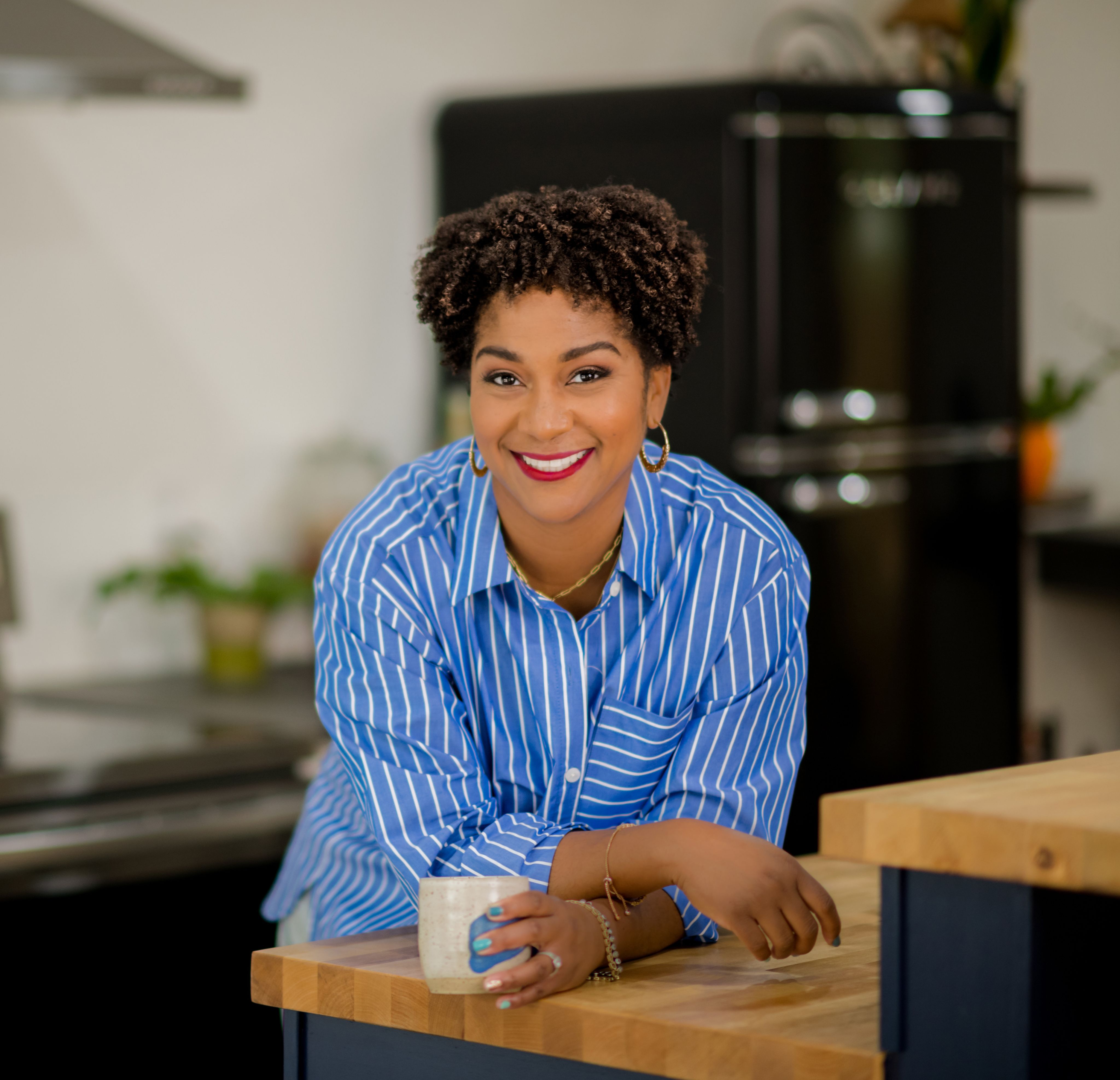 Erayna Sargent in blue and white striped shirt leaning on kitchen counter holding mug