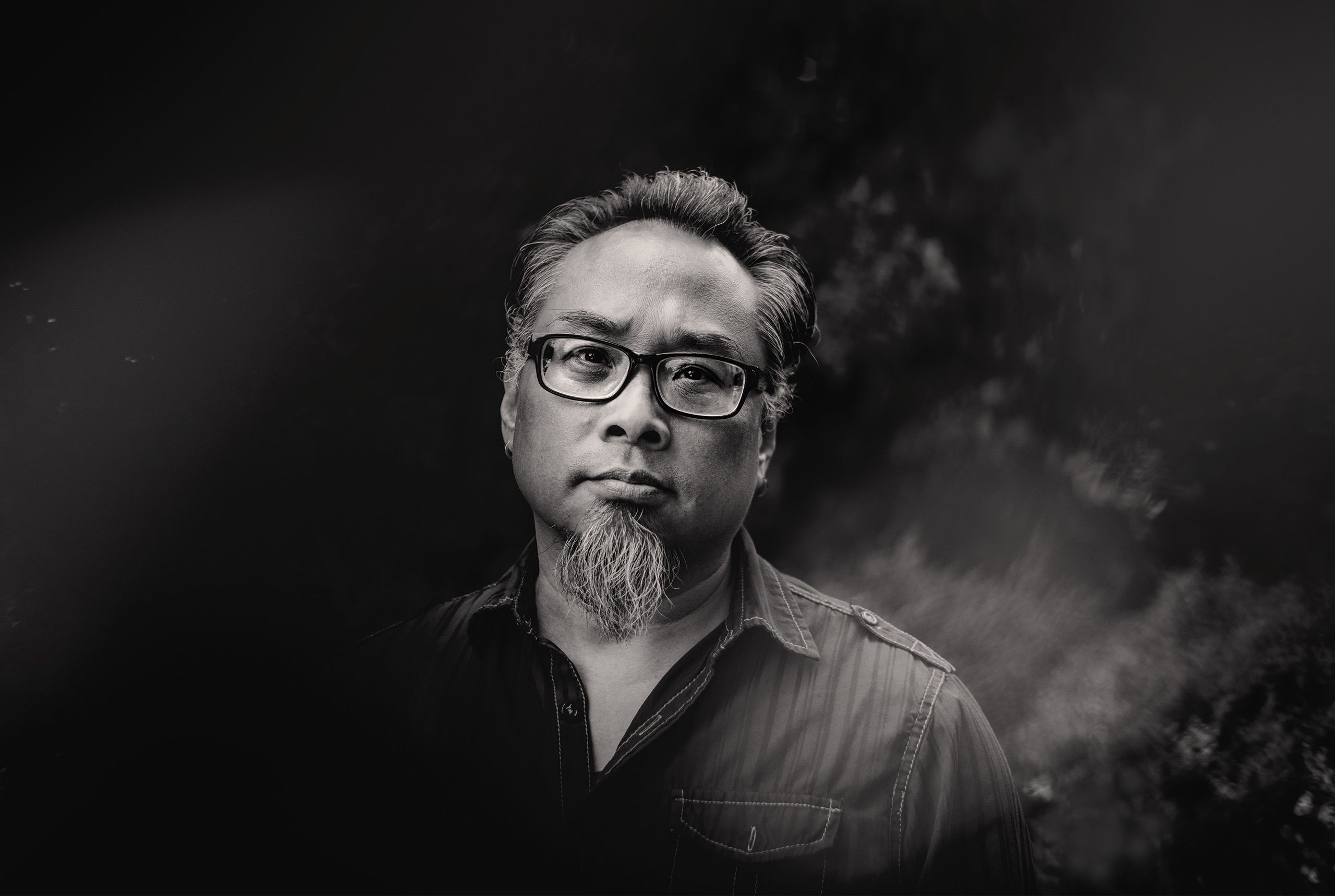 Todd Kaneko in black and white photo, with glasses and gotee, standing outside