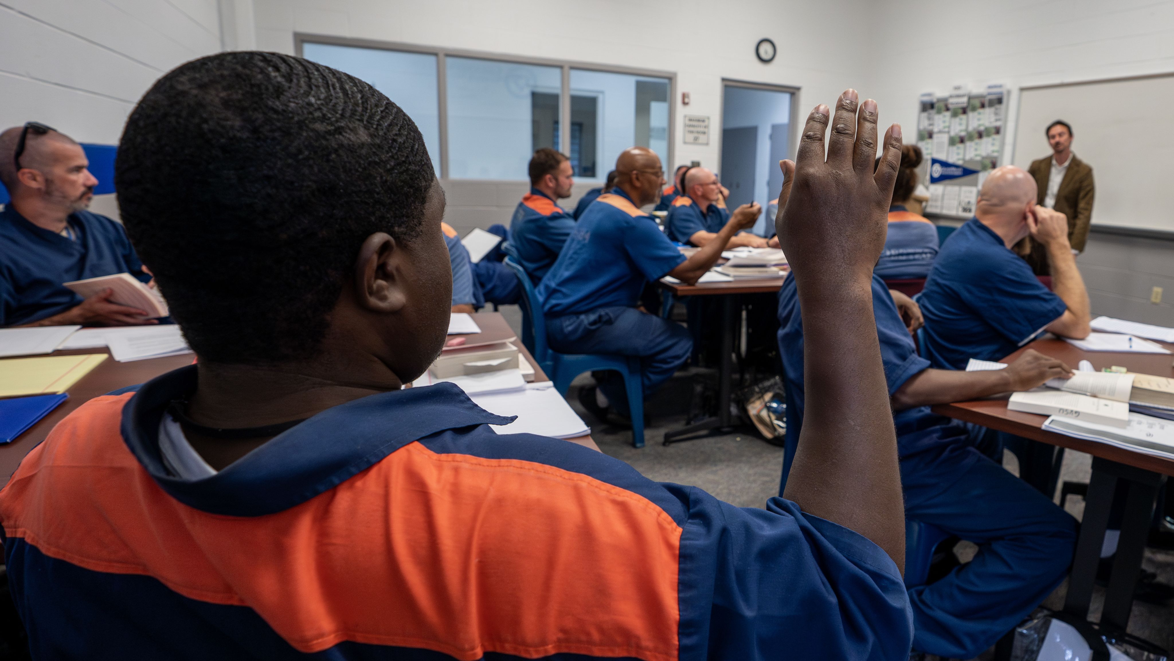inmate raises hand from back of room, classroom of inmates in blue and orange uniforms