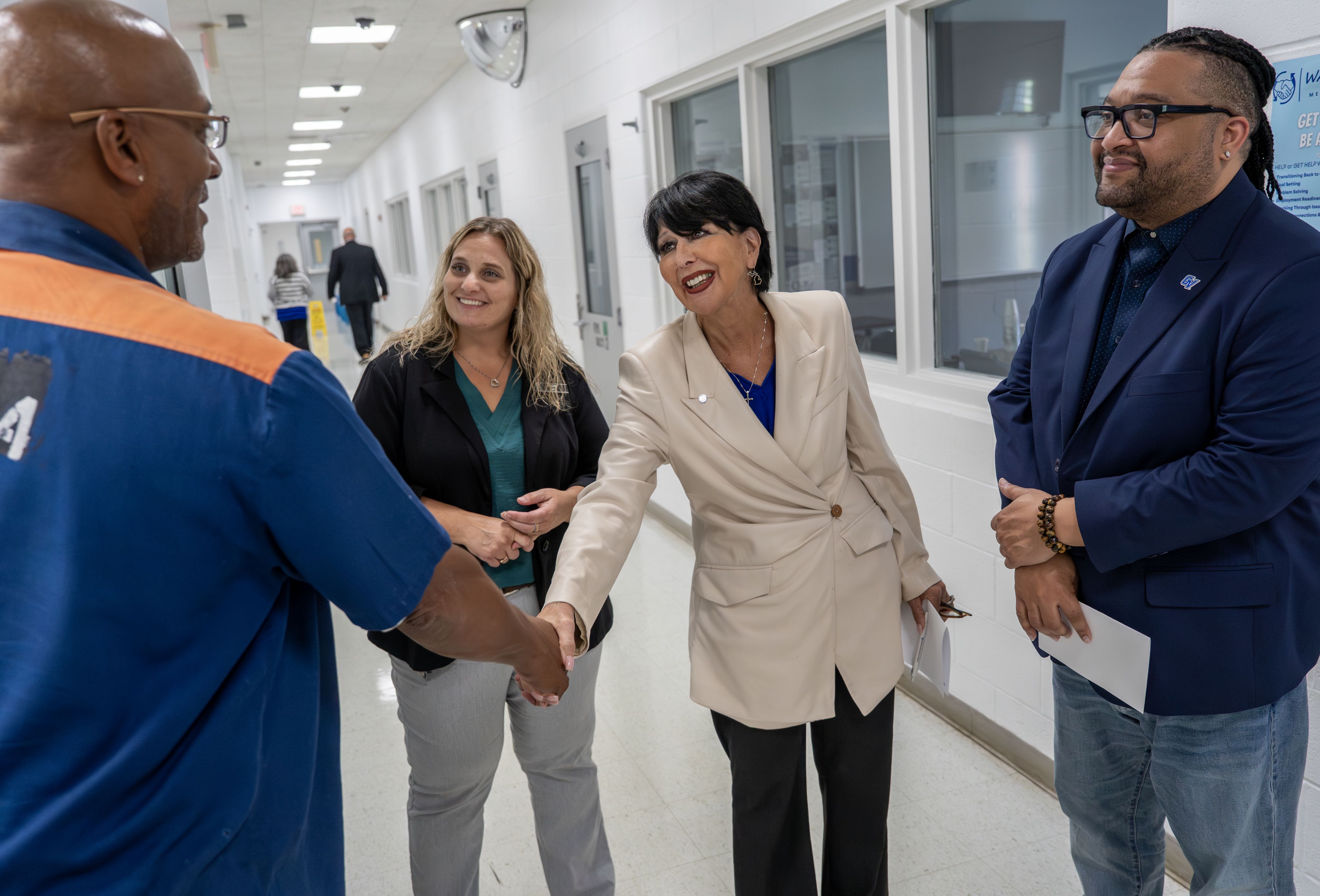 President Mantella shakes hands with an inmate while VP Robert Shorty at right, and another woman look on smiling