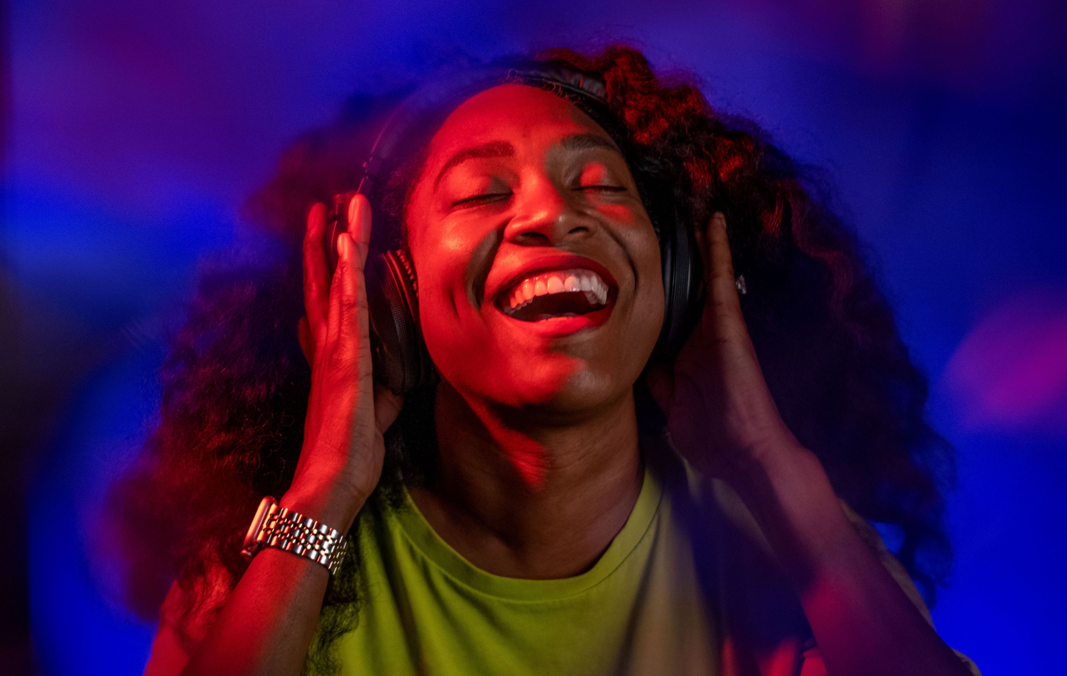 Andrea Wallace in yellow tshirt with headphones on, smiling; blue and purple background