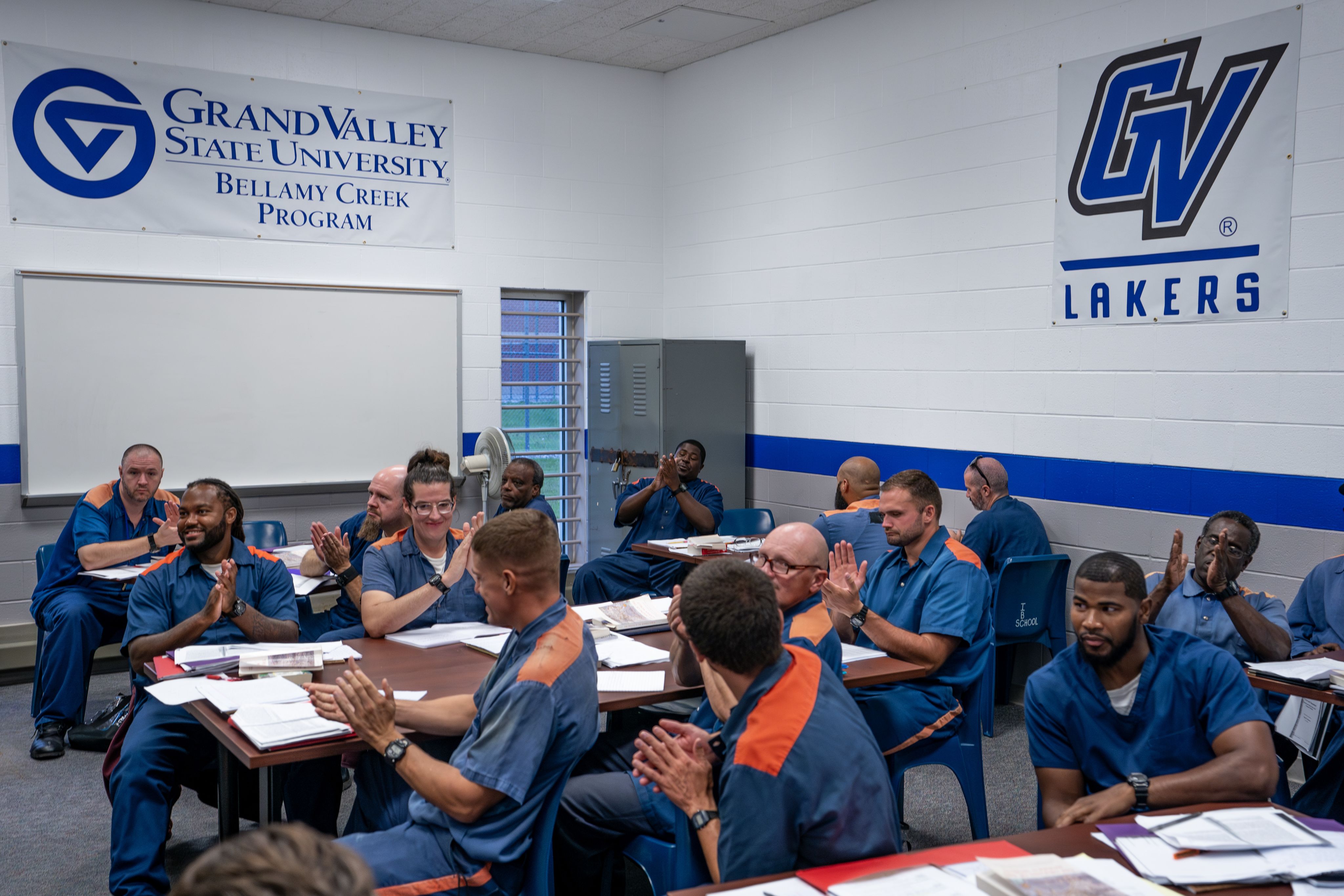 classroom with GV Lakes and GVSU Bellamy Creek Program banners on walls, inmates seated and most clapping