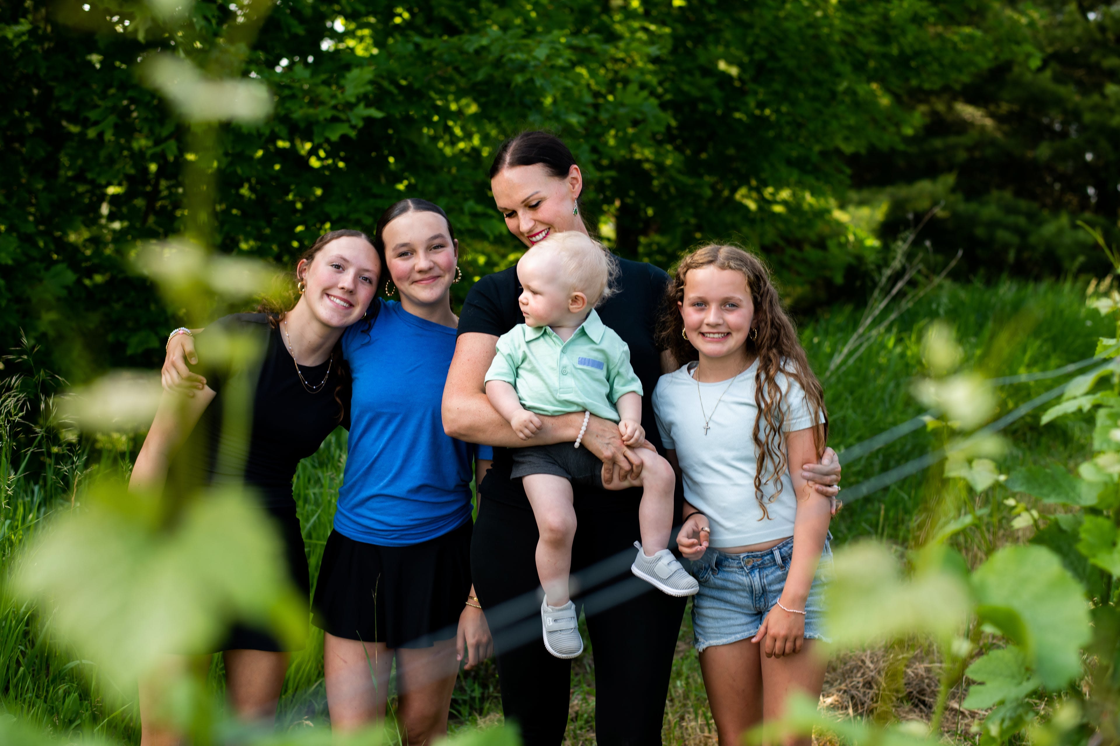 A mother stands close with her children outside in the shad of some trees