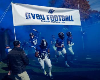 football players enter stadium under GVSU Football banner