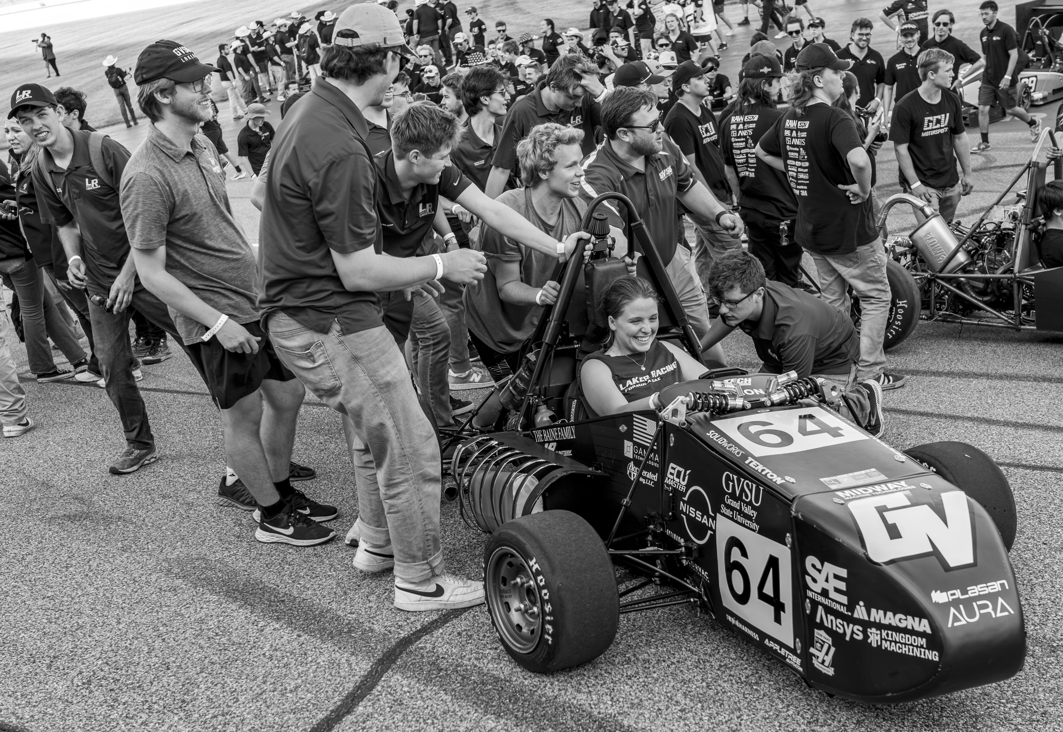A black and white photo of the laker racing car with a a driver and her team surrounding her