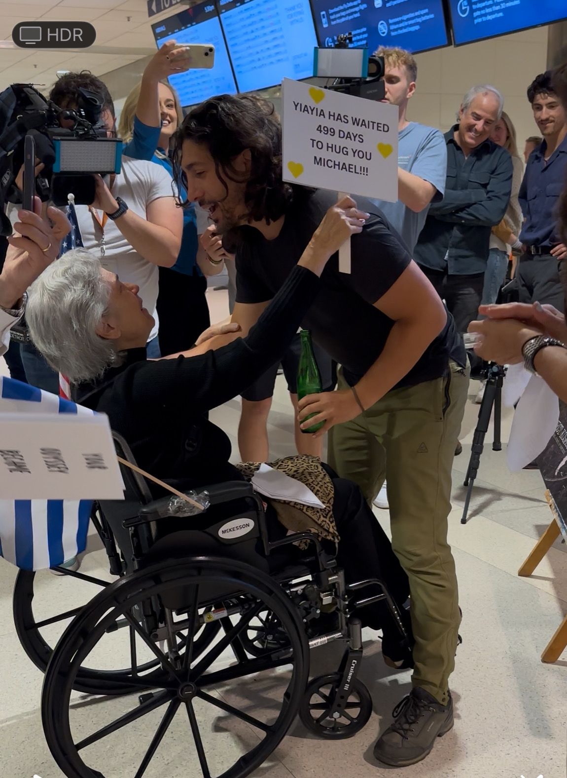 woman in wheelchair hugs Michael Zervos at the Detroit airport, other people in background