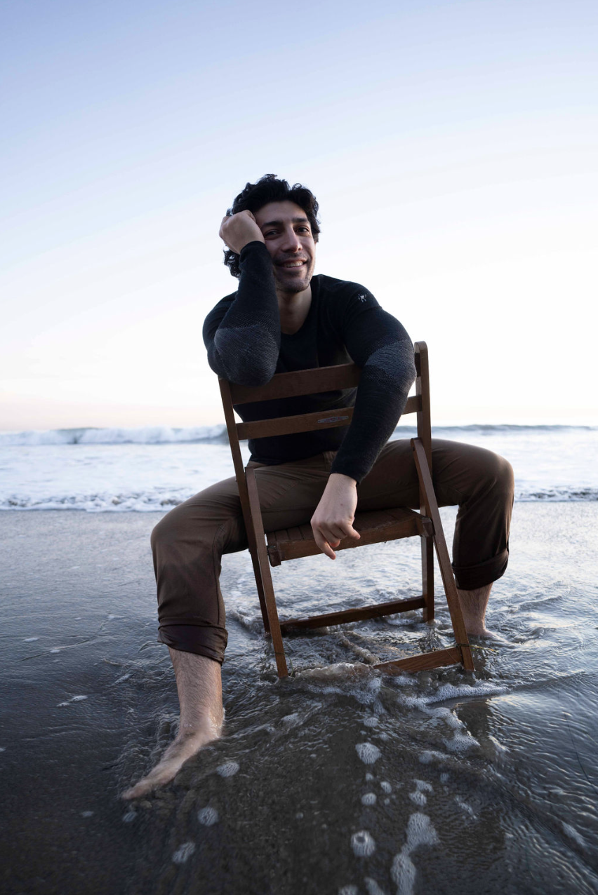 Michael Zervos in water near shoreline sitting on a wooden chair