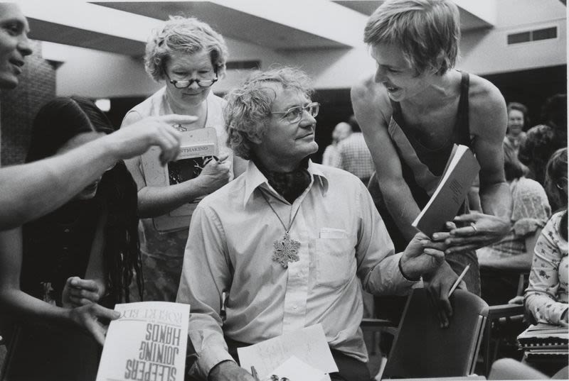 black and white photo of man seated while others crowd him at 1970s poetry festival