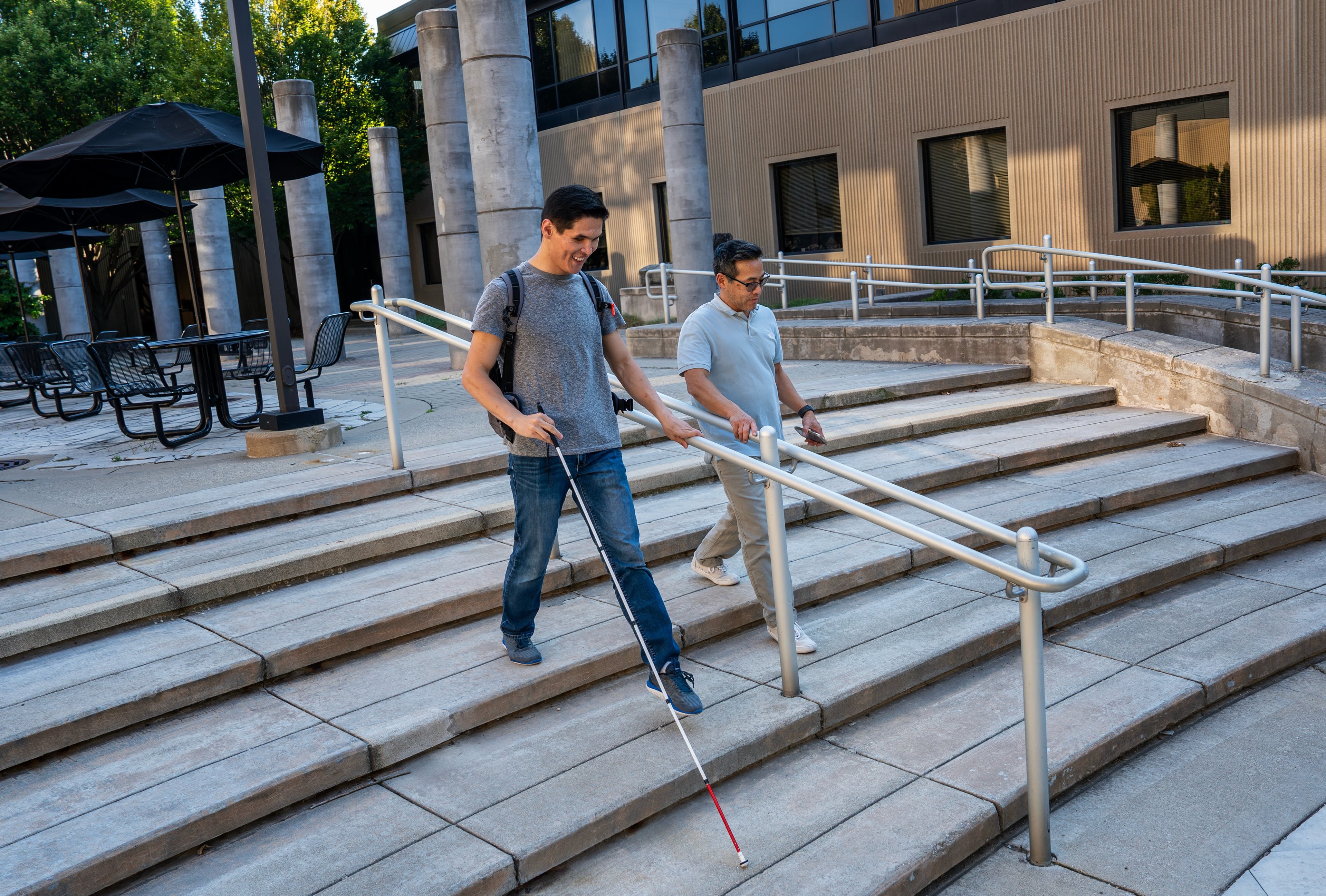 two people walking down stairs, person on left with white cane