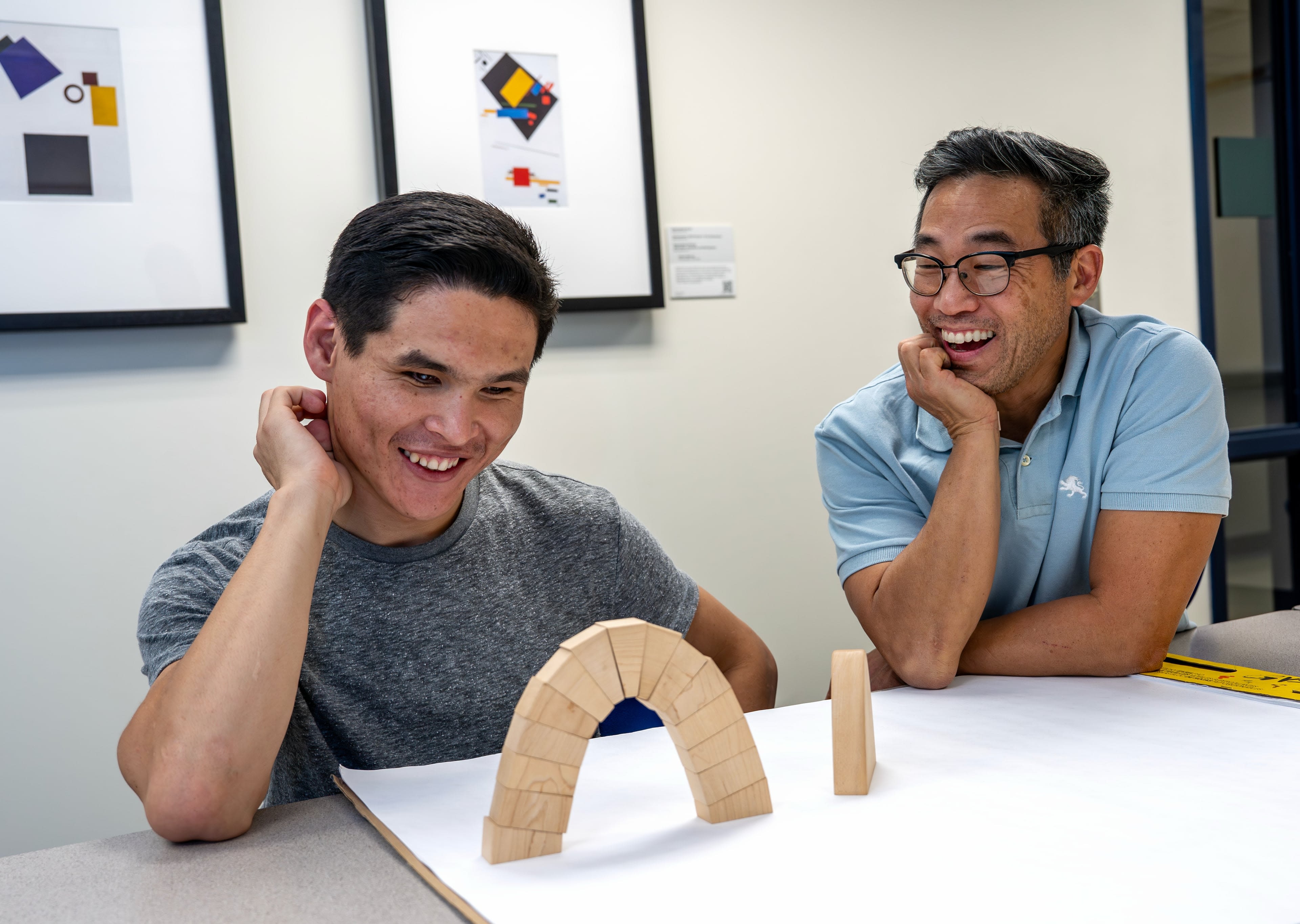 two people seated at table looking and smiling at symmetrical blocks to build a parabolic arch