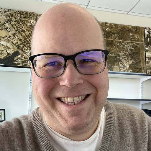 Josh Isaak in tan sweater, glasses, smiling 