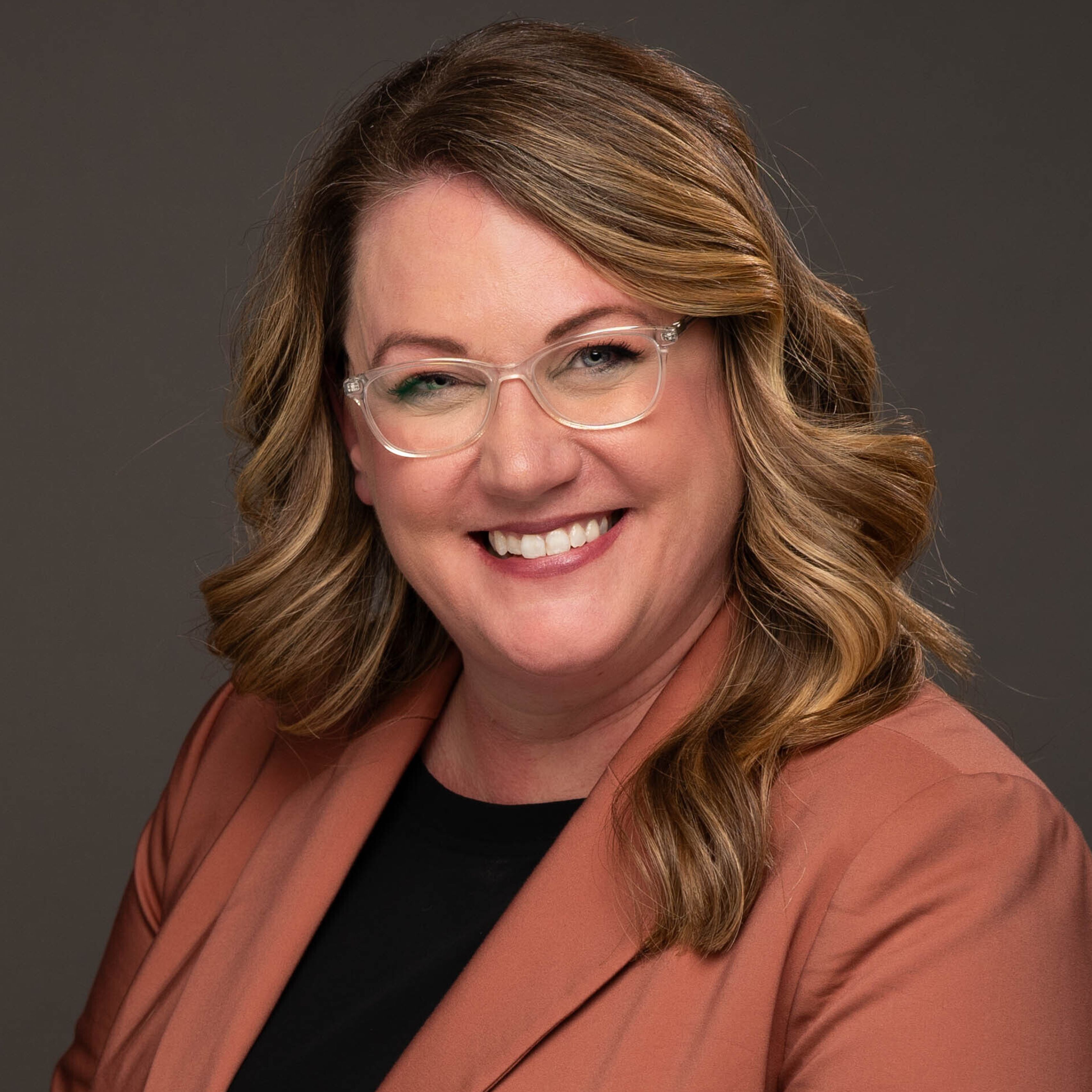 Elizabeth Lienau in orange blazer, glasses, smiling