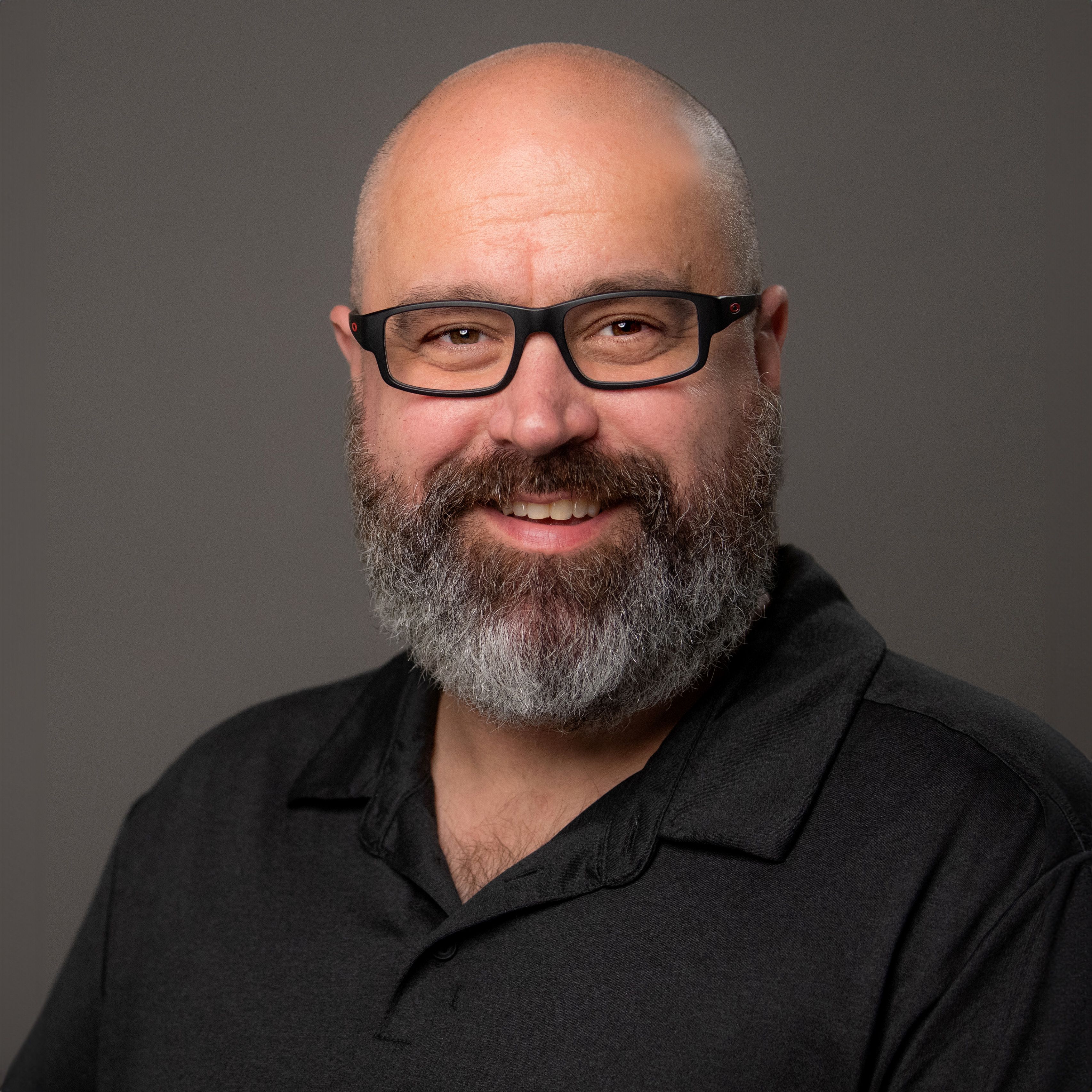 Cory Morse, in a dark shirt and black frame glasses, smiling
