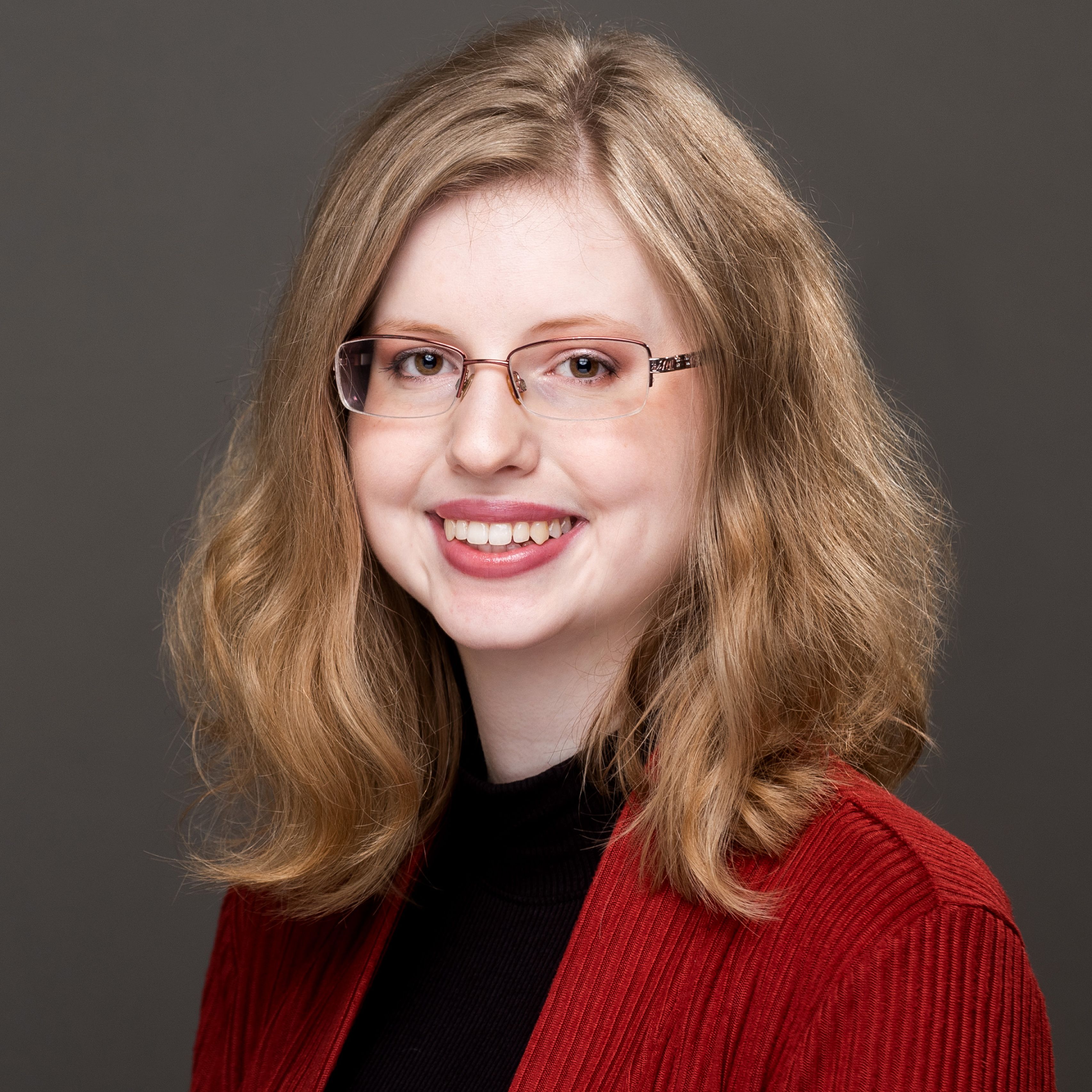 Katherine Barnard in red sweater, glasses, smiling
