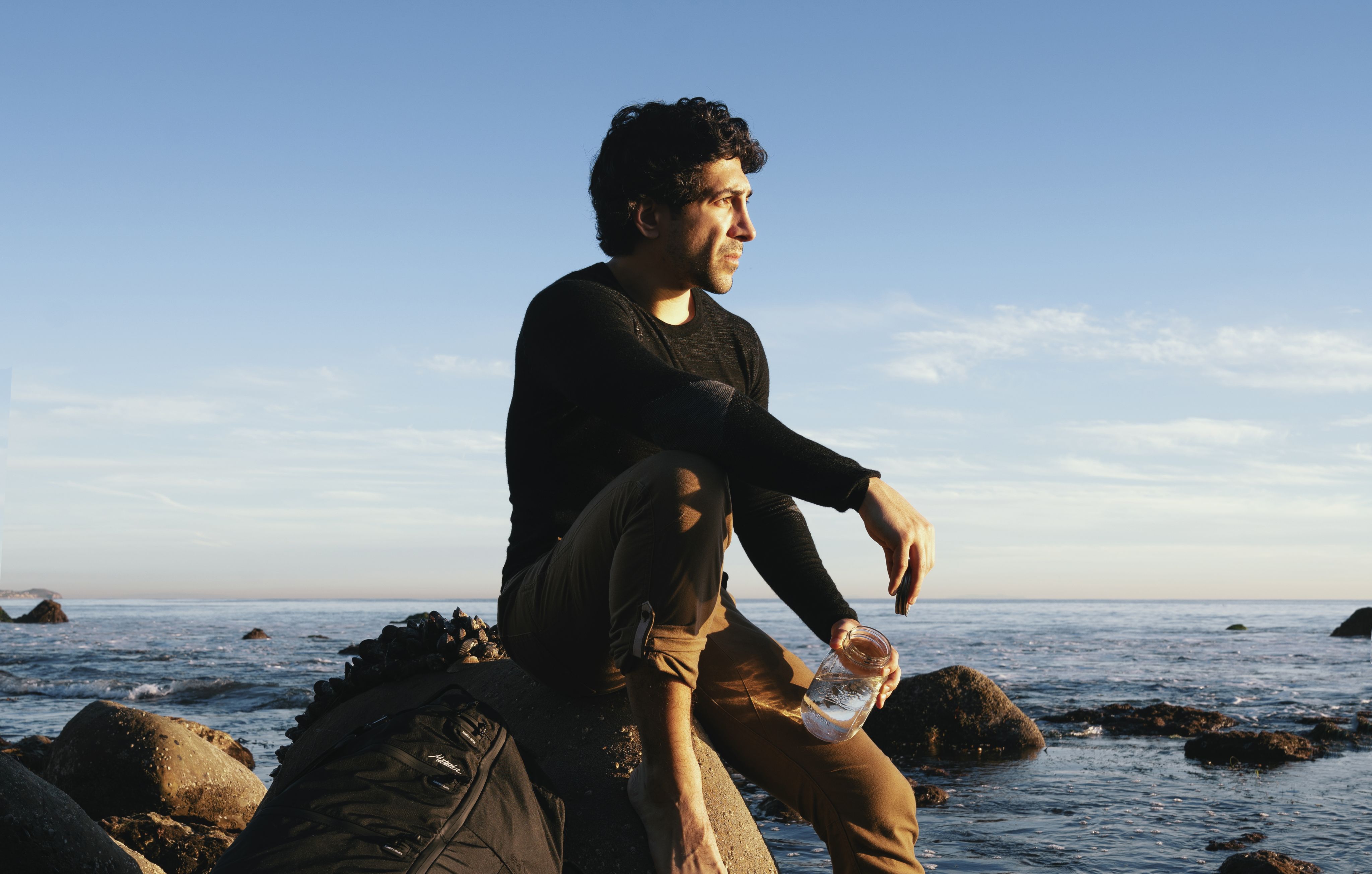 Michael Zervos sits on a rock in the Pacific Ocean