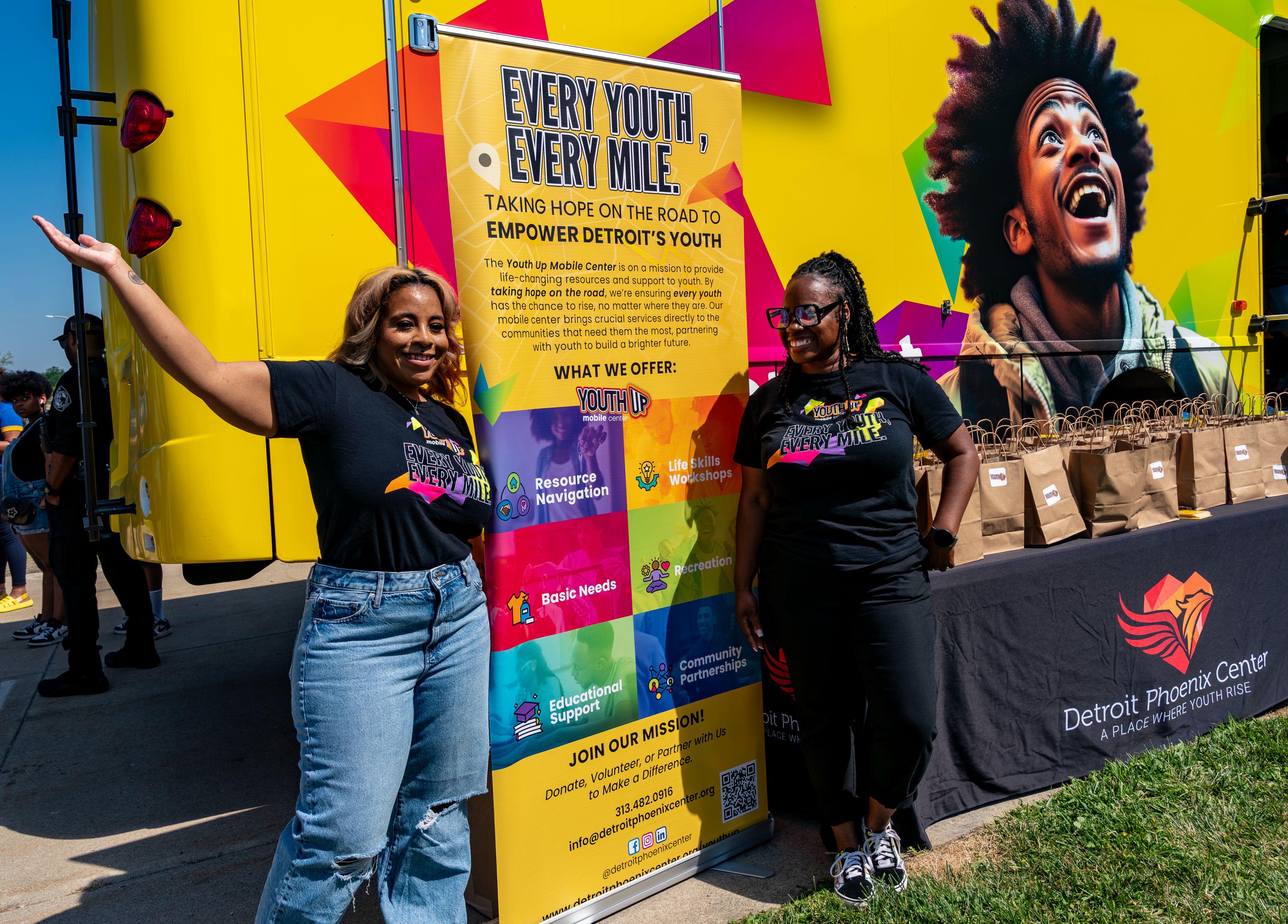 two women stand on either side of a vertical banner near truck, Every Youth, Every Mile on top of banner