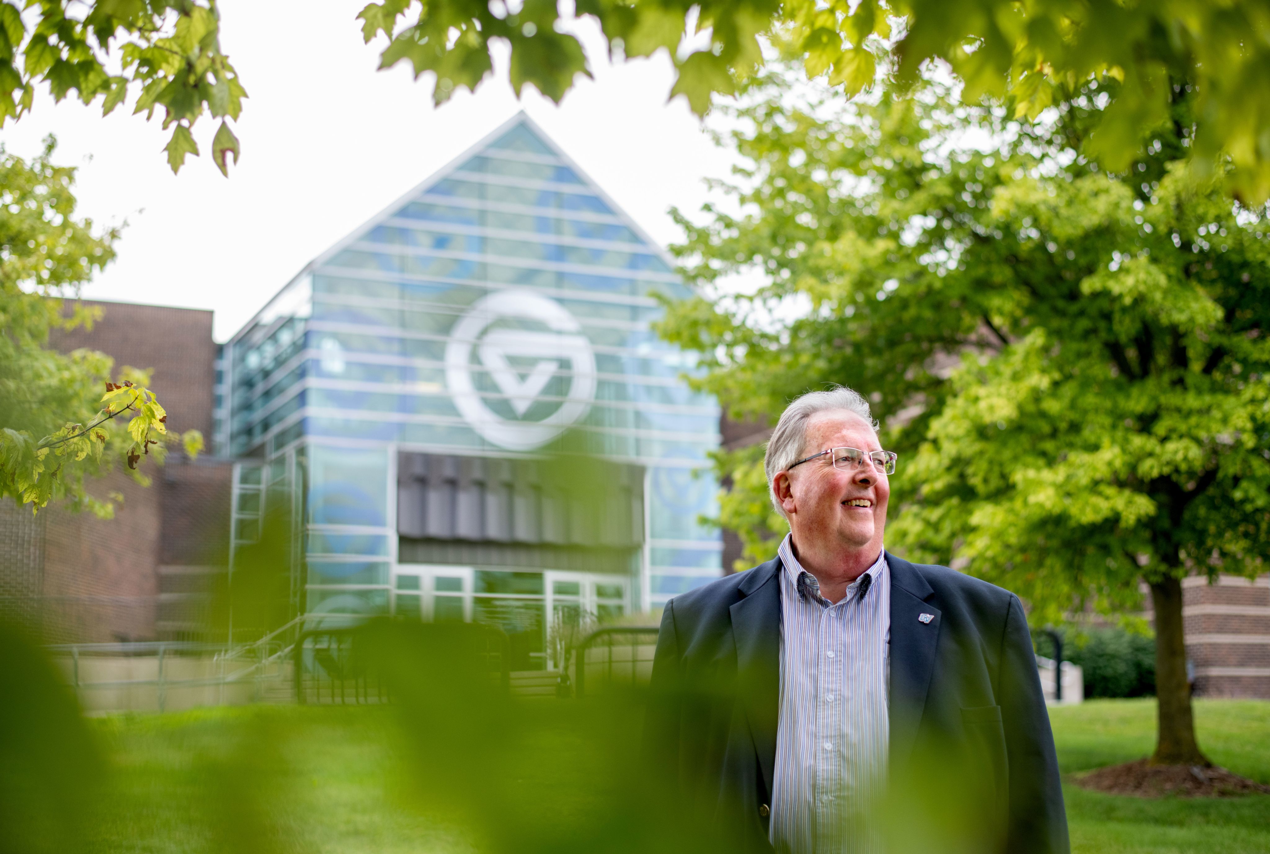 Bob Stoll stands outside the Kirkhof Center, circle GVs on building glass