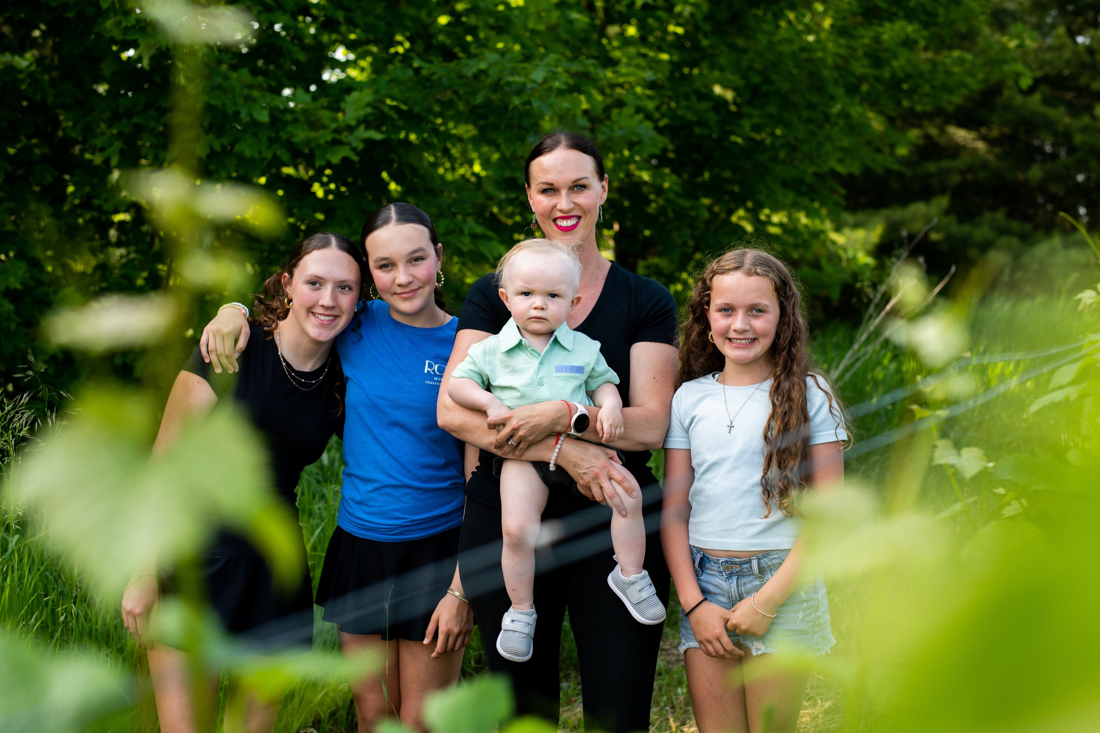 A woman stands with her 4 children in the shade of some trees