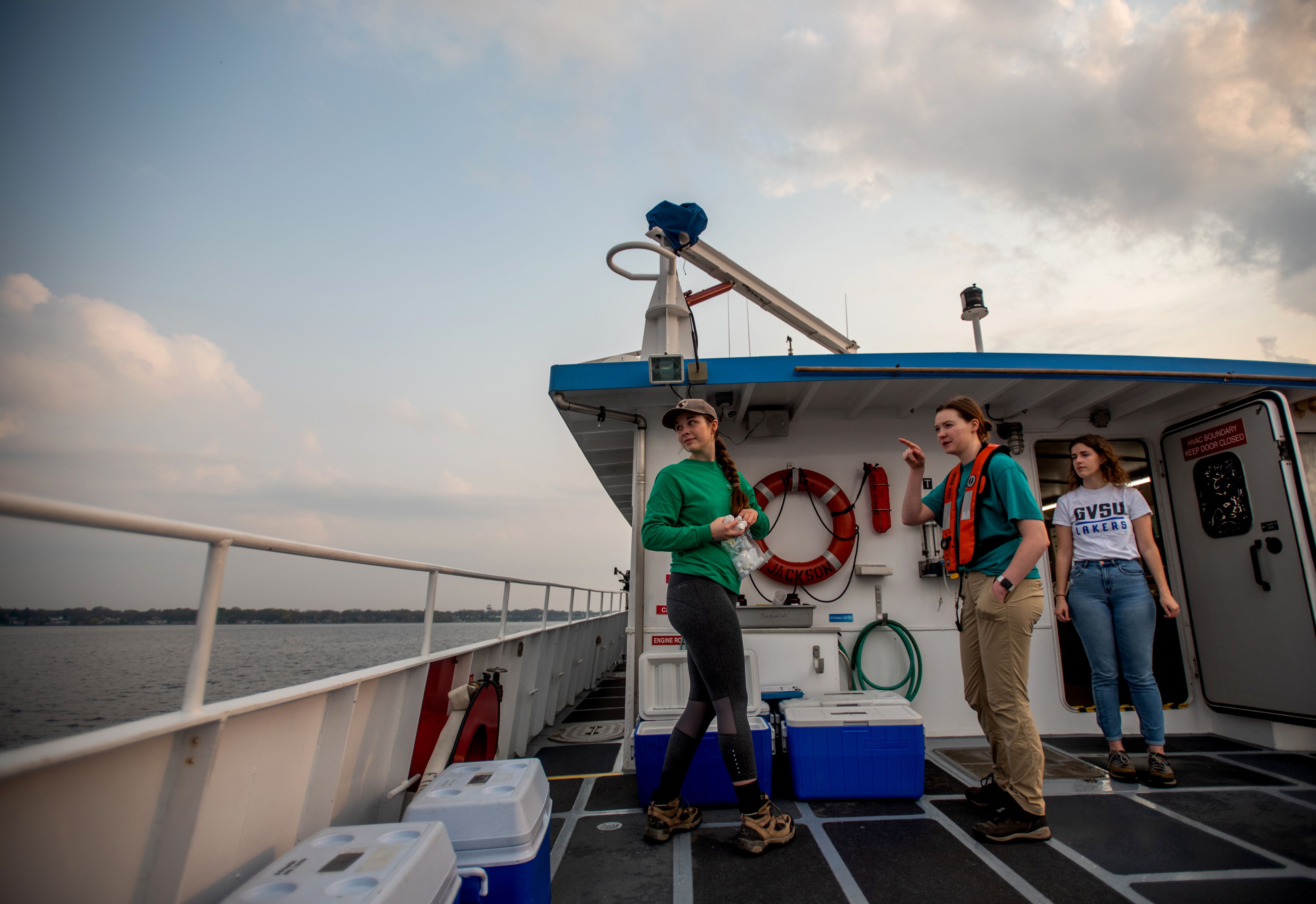 three students at the back end of a boat, on deck