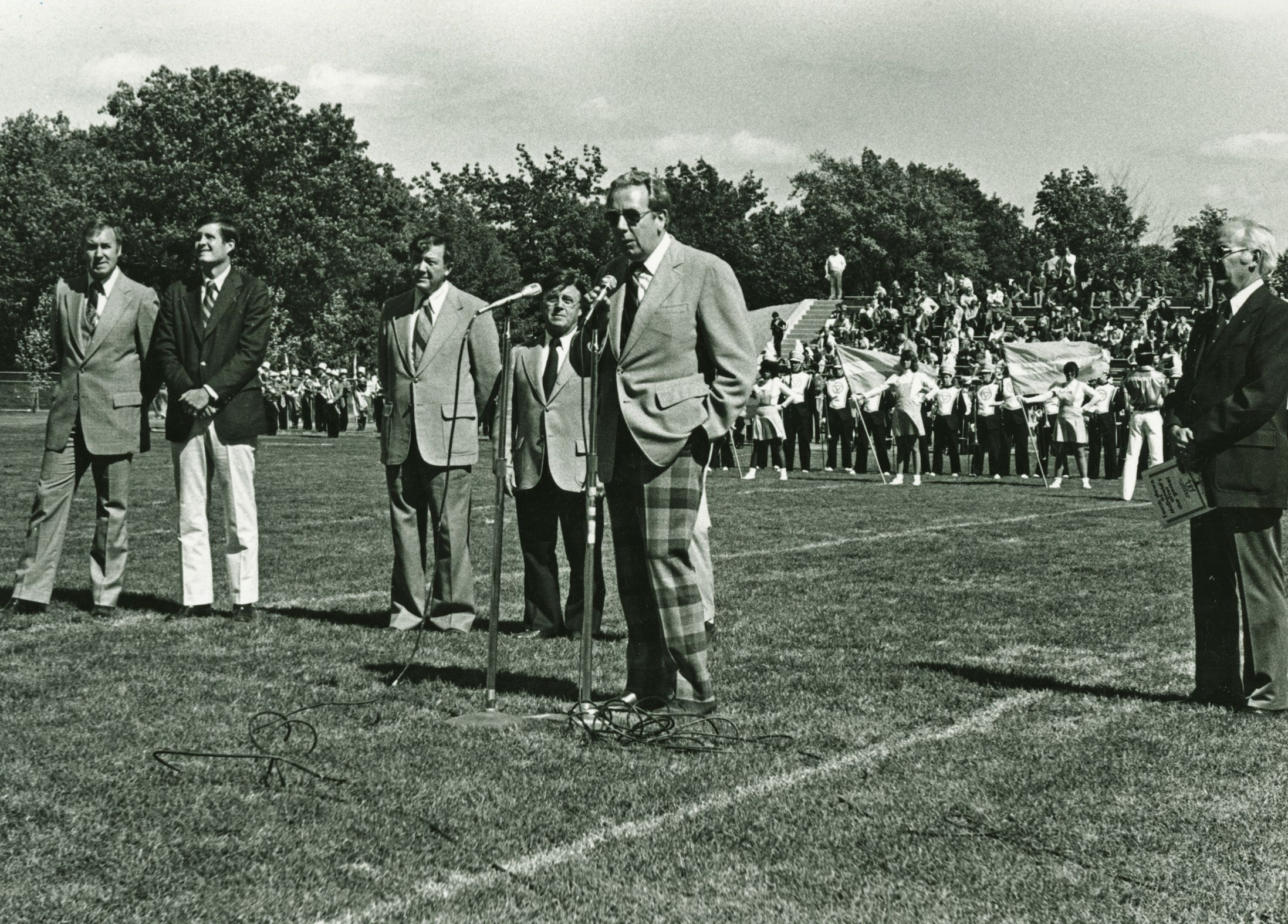 in 1979, man in plaid pants speaks into a microphone on a football field