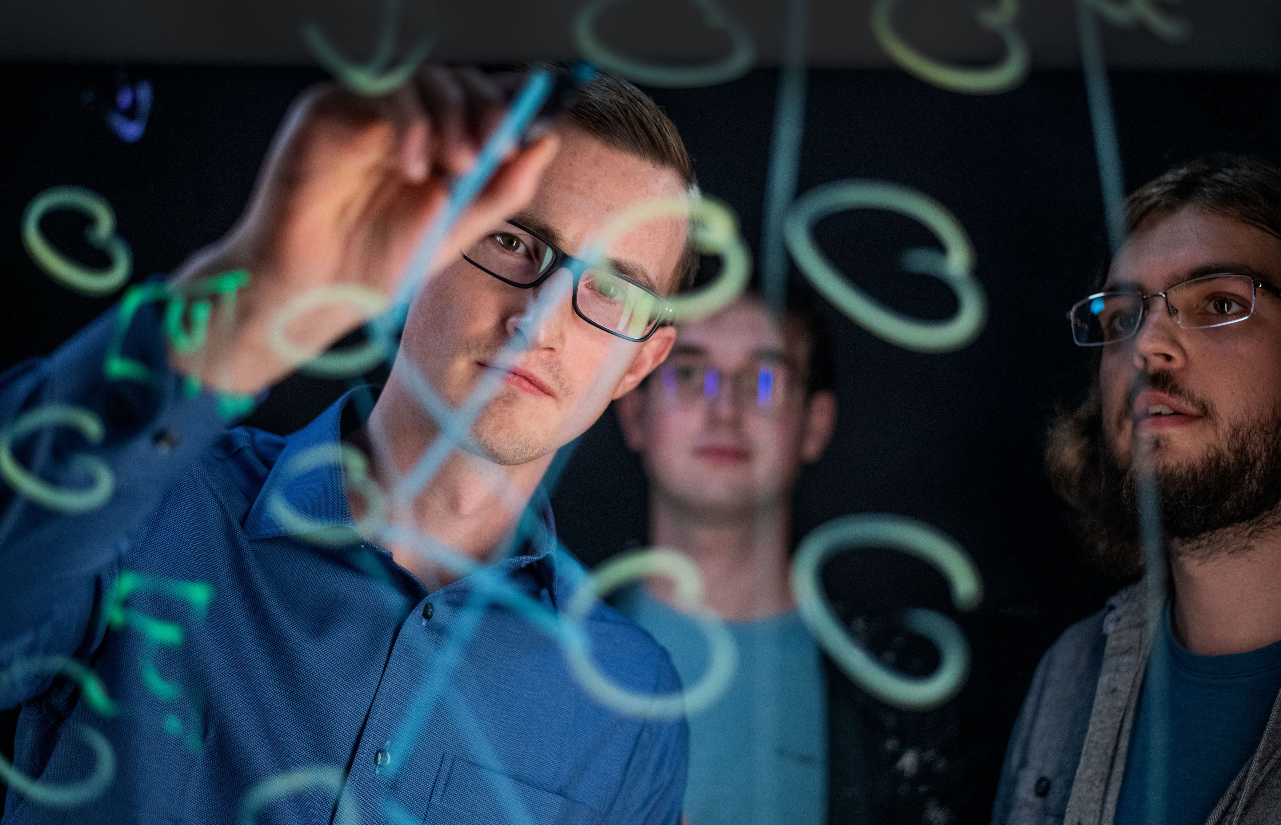  Zach DeBruine holds marker to clear writing board, drawing figures and shapes, he is wearing a blue button down shirt