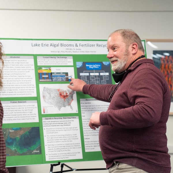 A person points to a spot on a board containing information on research on Lake Erie algal blooms while talking with others.
