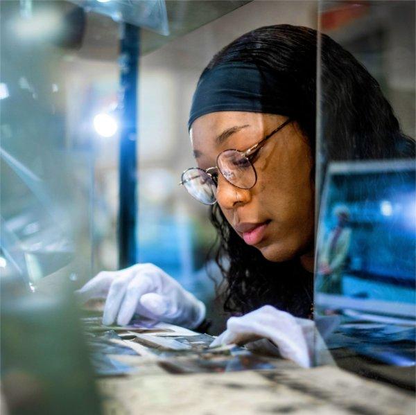 Jada Dobbins is wearing gloves while looking at old photos at the GRAAMA.
