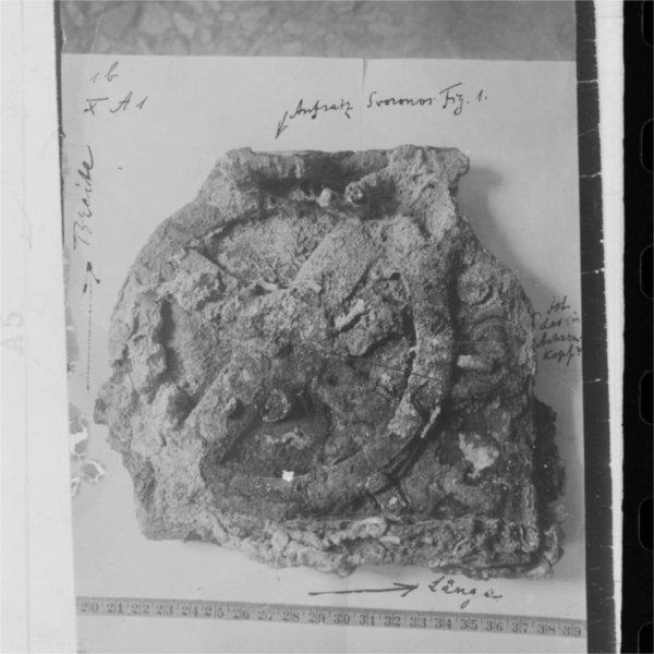 A black and white photo shows an artifact that appears to have a dial on it. There is also some writing on it.