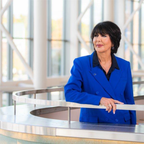 A person gazes to the side while resting an arm on a railing.