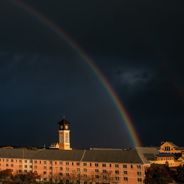 A rainbow is seen against a dark stormy sky in front of a college campus