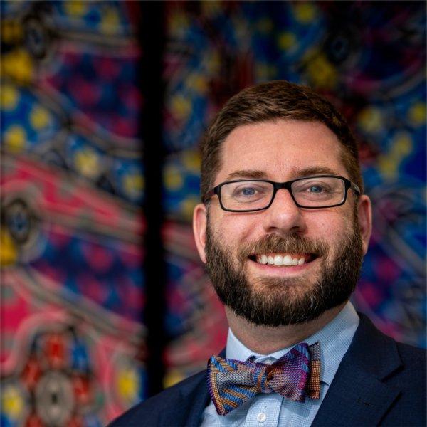 Kyle Kooyers standing in front of colorful artwork that reflects his bow tie