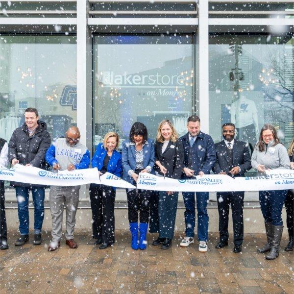 A group of people stand outside a modern building cutting a ribbon with scissors.