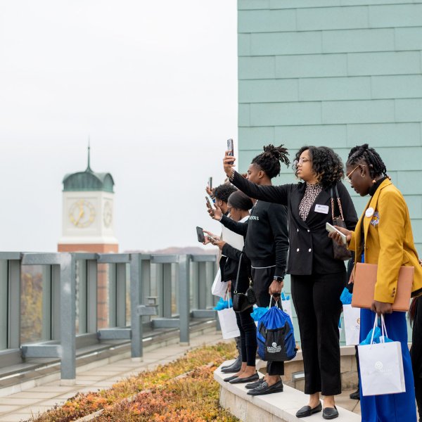 students stand on fourth floor balcony of Pew Library and take cell phone photos