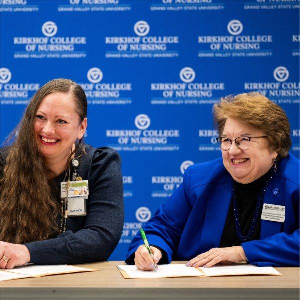 Maria Opoku�Agyeman, left, and Linda Lewandowski smile and sign papers in front of a KCON backdrop