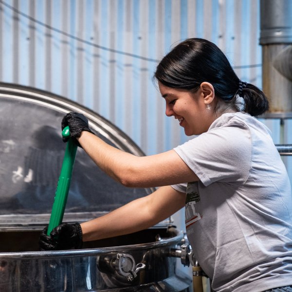 A person smiles while stirring in a large kettle.
