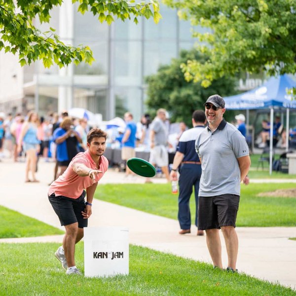 student throws disc while one person looks on on lawn in front of Pew Library on the Allendale Campus