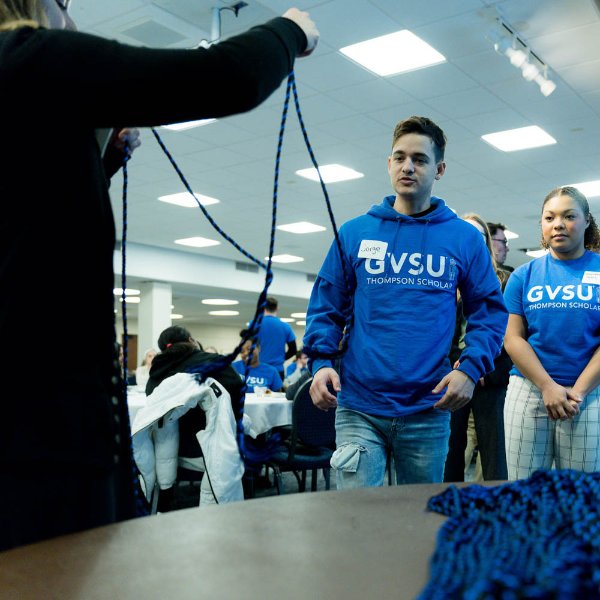 students in blue t-shirts with GVSU Thompson Scholars stand in line to receive graduation cords, which are blue