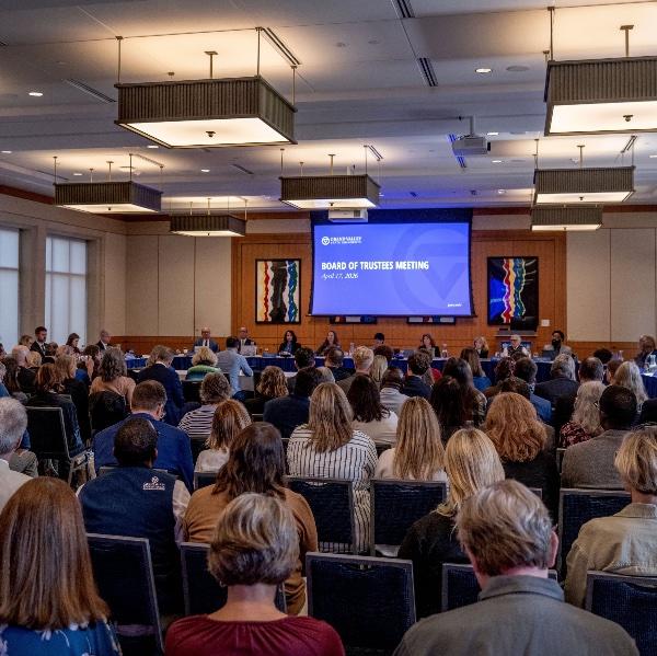 Audience members shown from behind seated in a room facing the GVSU Board of Trustees