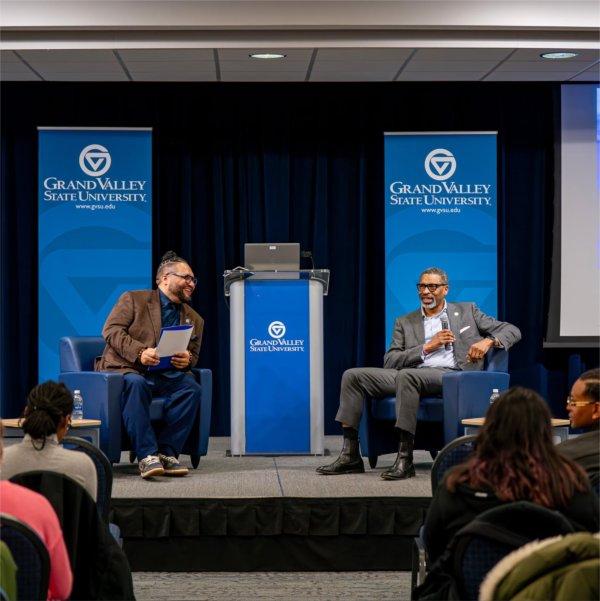 Robert Shorty, left, and Derrick Johnson on stage seated in the Kirkhof Center, GVSU vertical banners behind them